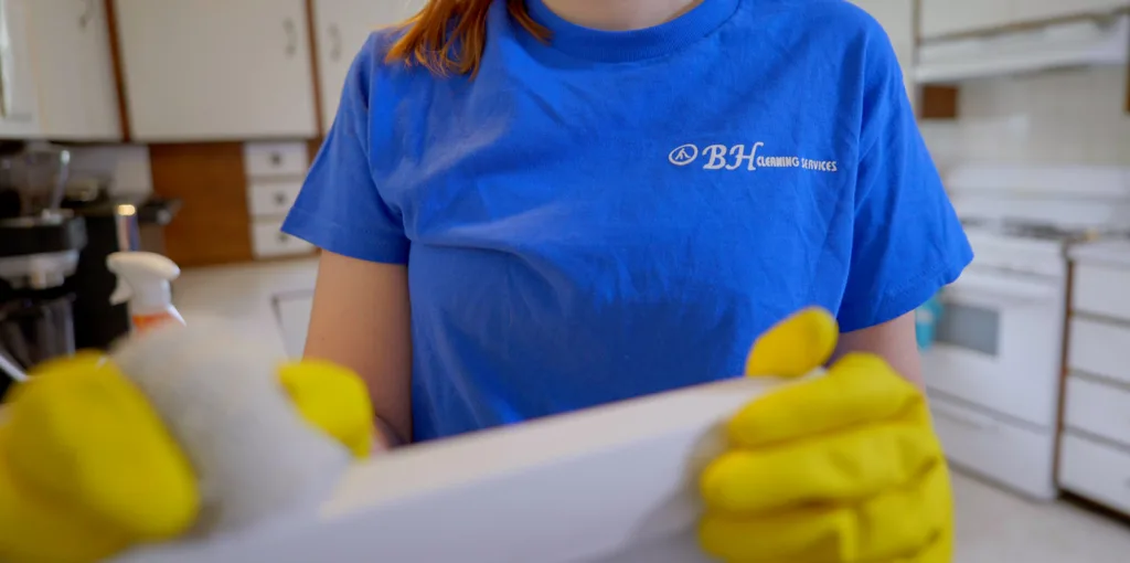 A close up shot of hands cleaning a microwave door with the shirt logo in view.